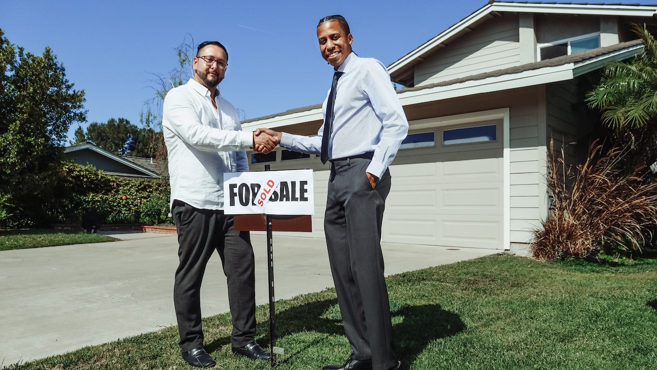 Two men shake hands in front a home.