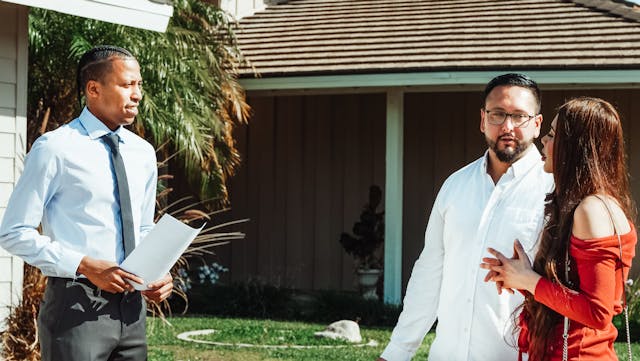 Real estate agent with documents talking to a potential buyer outside a house.