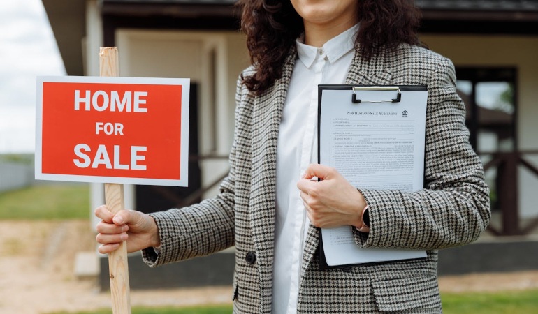 Woman holding a "home for sale" sign