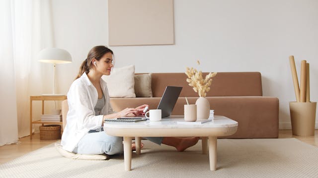 A girl sitting on the floor at a coffee table working on a laptop